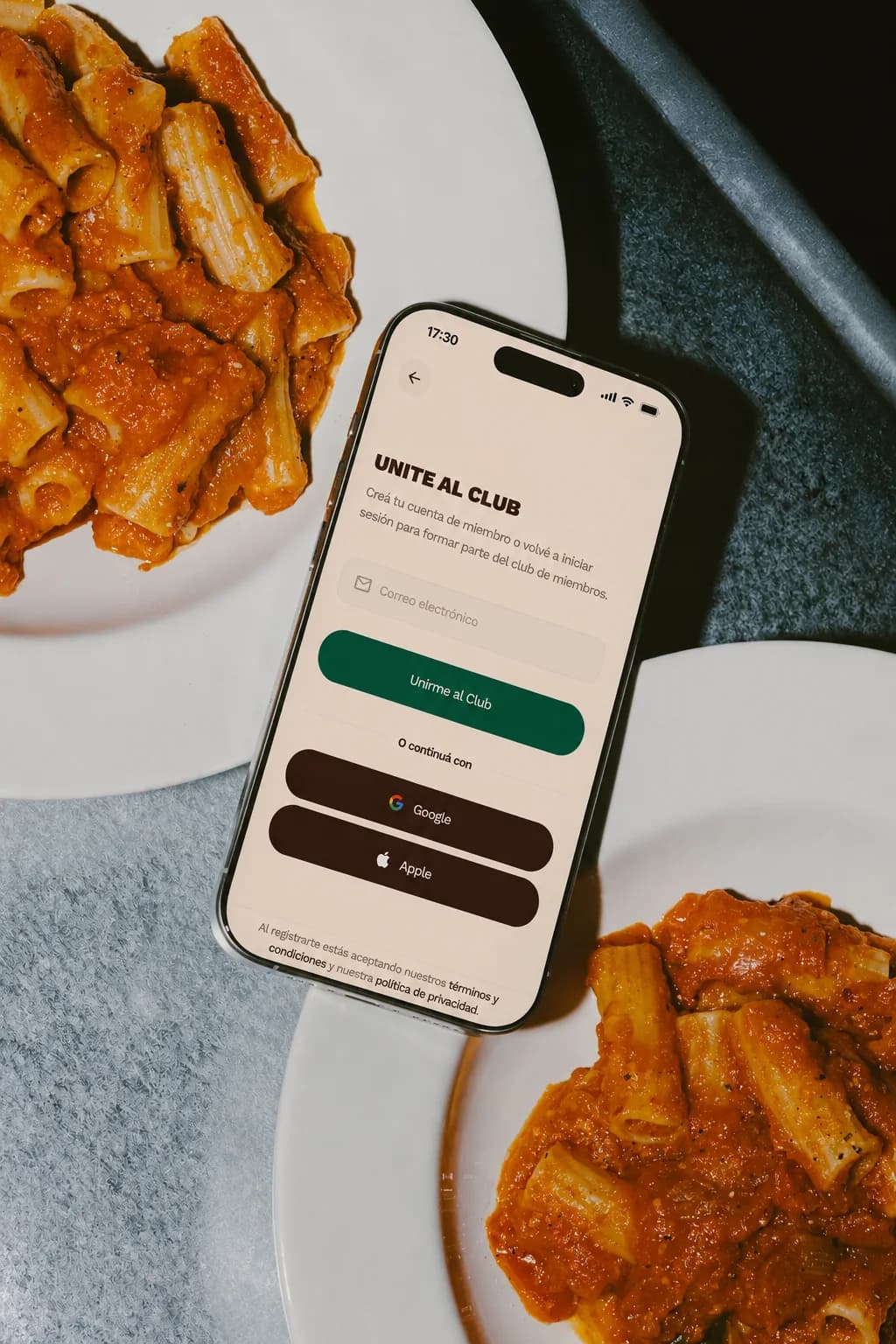 Un teléfono con la pantalla de alta al club apoyado entre dos platos de pasta