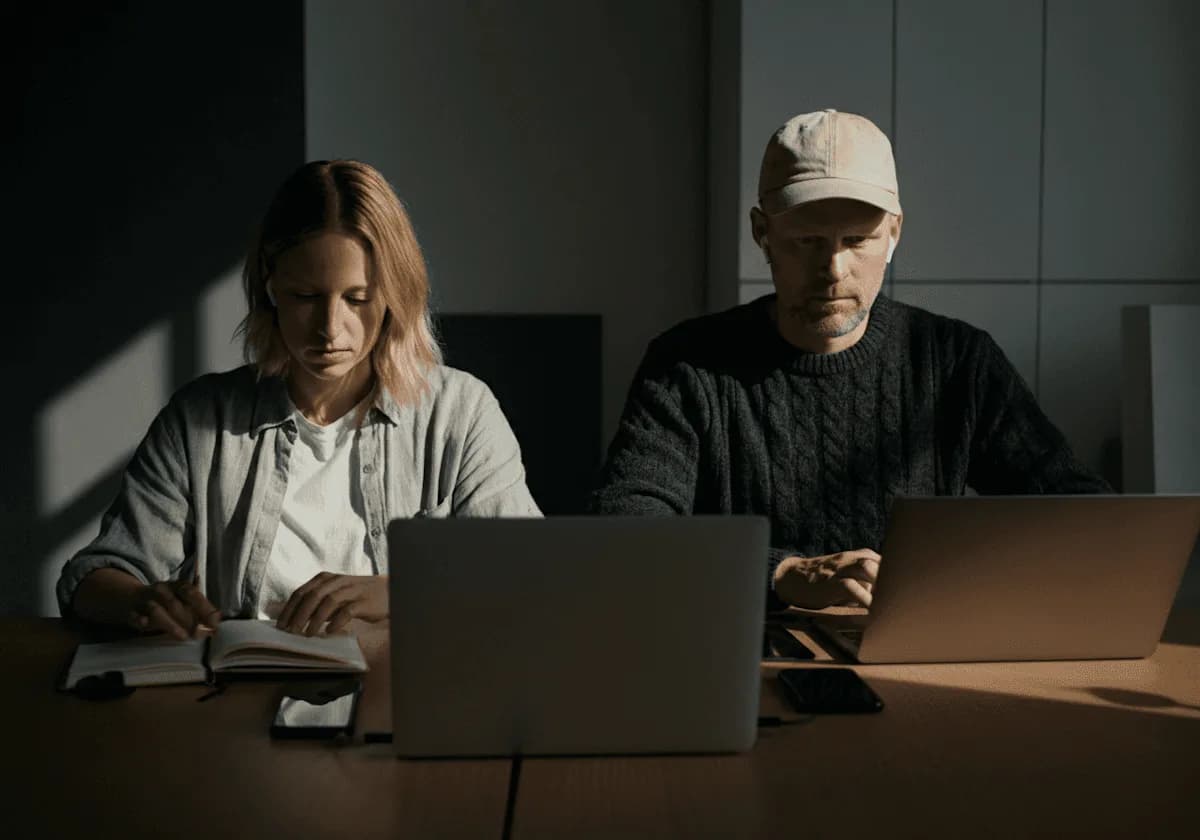 Dos personas trabajan con sus laptops en una oficina en penumbra