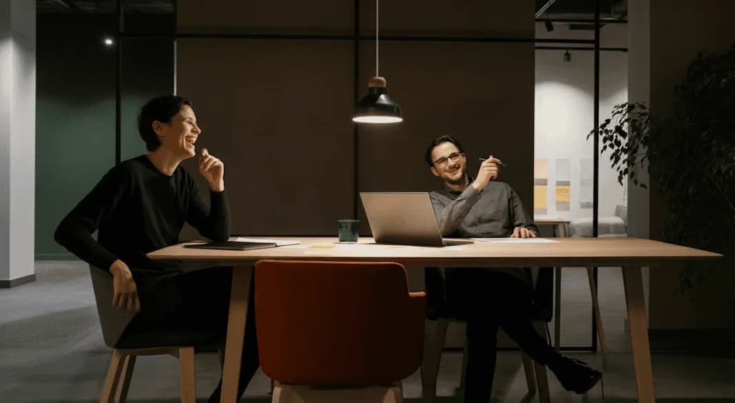 Dos personas conversan sentadas en una sala de reuniones en penumbra