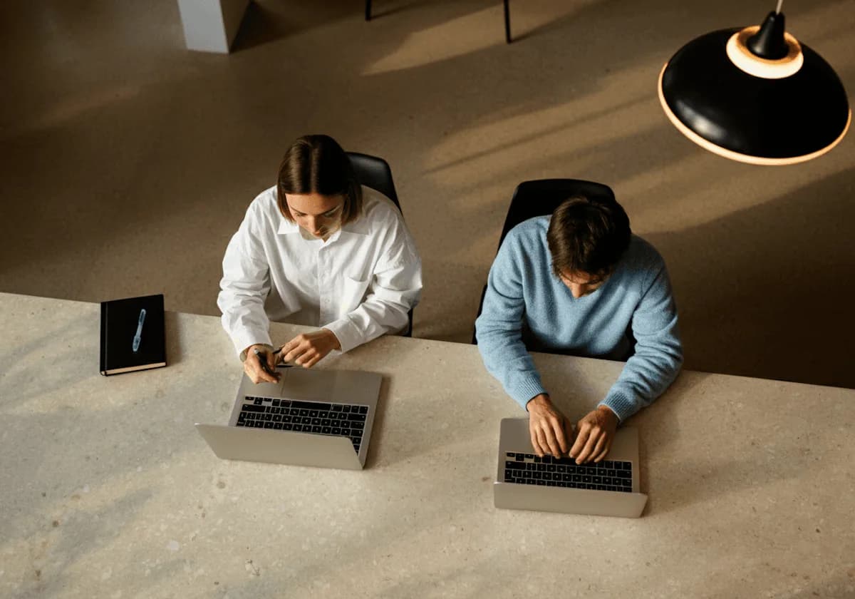 Dos personas trabajan con sus laptops en un escritorio compartido
