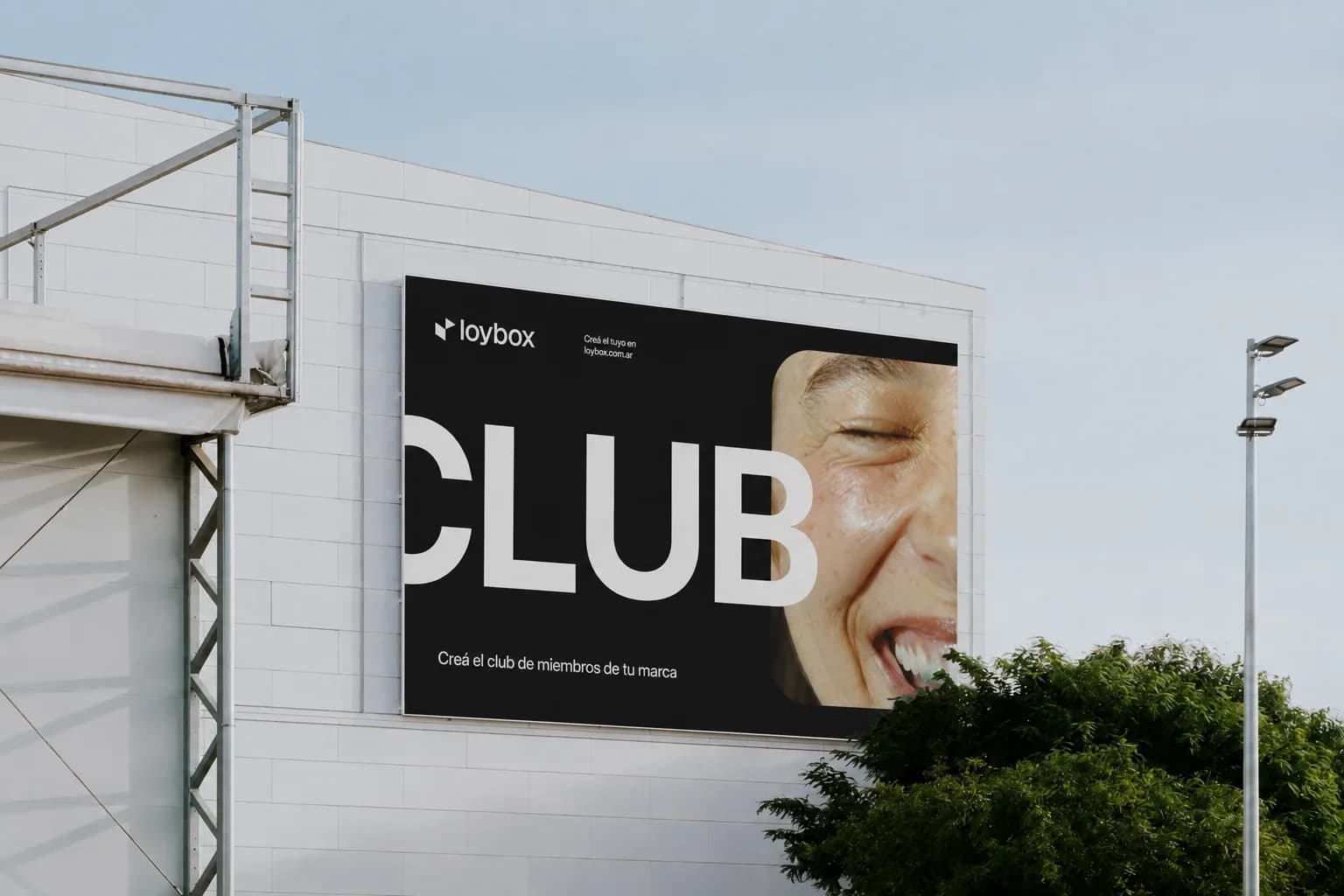 A Loybox billboard on the facade of a building: the word CLUB in giant letters next to the photo of a woman laughing, and below it “Creá el club de miembros de tu marca”