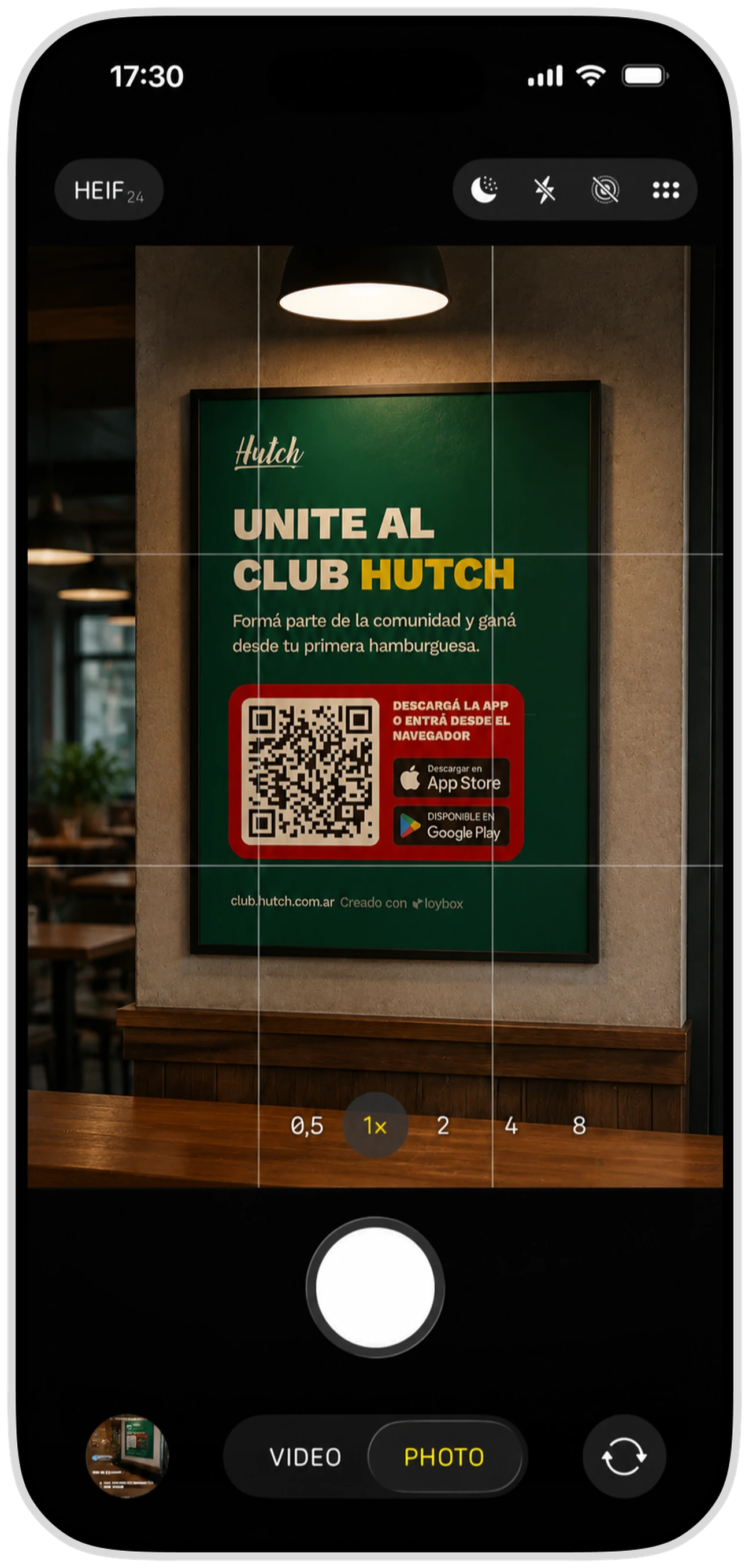 La cámara del iPhone enfocando el cartel del Club Hutch colgado en el local, con el QR y los sellos de las dos tiendas
