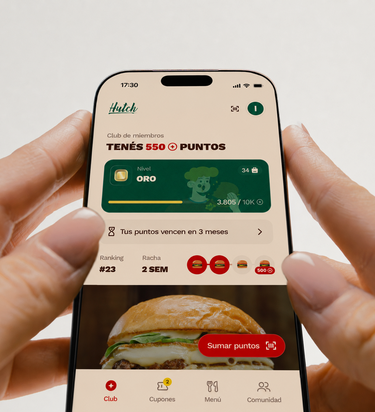 Dos manos sosteniendo un teléfono con la app del club de Hutch: 550 puntos, nivel Oro, la racha de dos semanas y el botón para sumar puntos