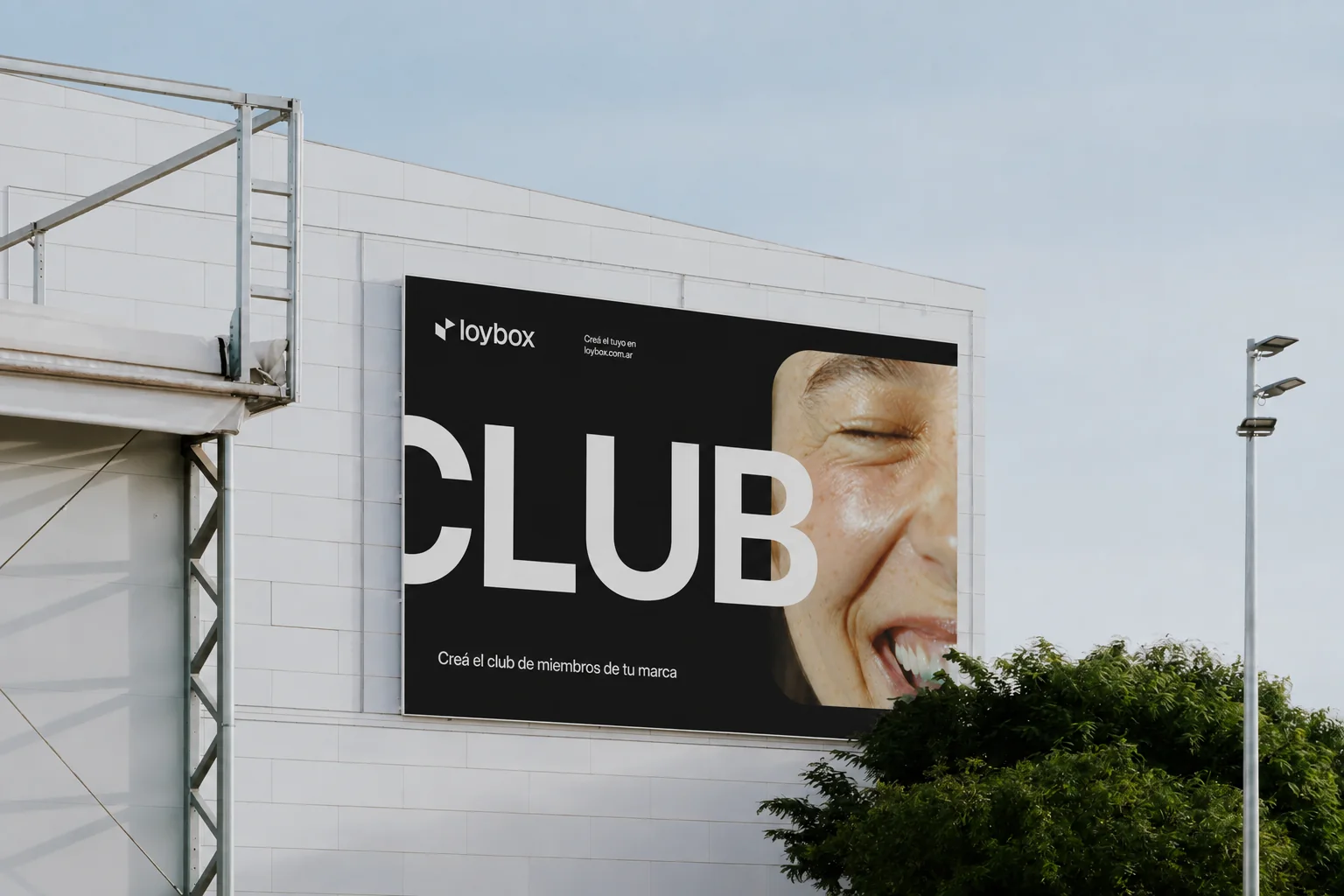 Una cartelera de Loybox en la fachada de un edificio: la palabra CLUB en letras gigantes junto a la foto de una mujer riéndose, y abajo “Creá el club de miembros de tu marca”