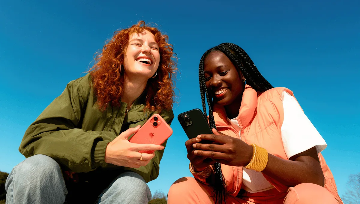 Dos mujeres sentadas al sol con sus teléfonos, contra un cielo azul