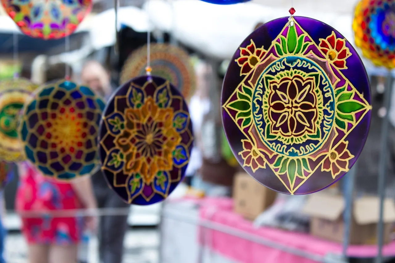 Mandalas de vidrio pintado cuelgan en un puesto de feria al aire libre mientras la gente recorre los pasillos