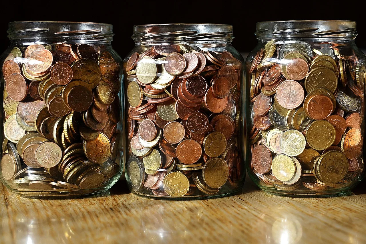 Tres frascos de vidrio llenos de monedas uno al lado del otro sobre una mesa de madera