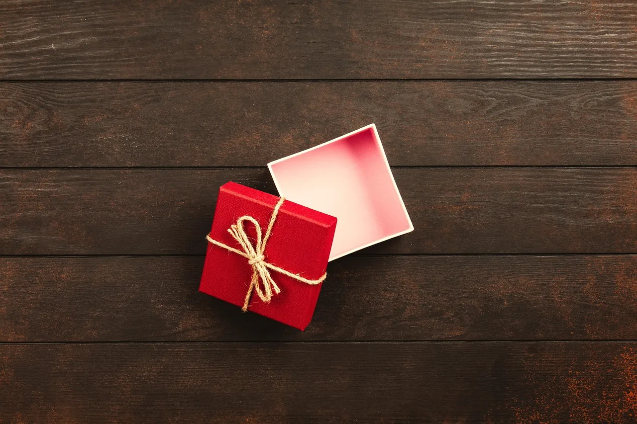 Una caja de regalo roja atada con hilo y su tapa abierta sobre una mesa de madera oscura