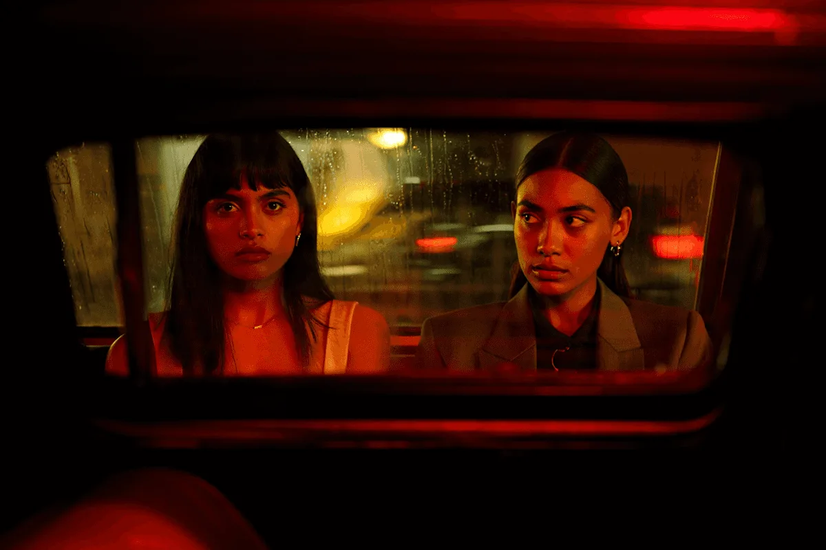 Dos mujeres dentro de un auto de noche, iluminadas por una luz roja