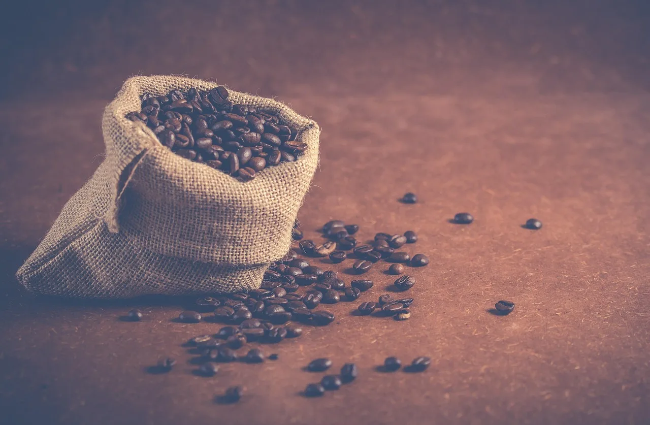 Una bolsa de yute abierta llena de granos de café con algunos granos sueltos sobre una mesa