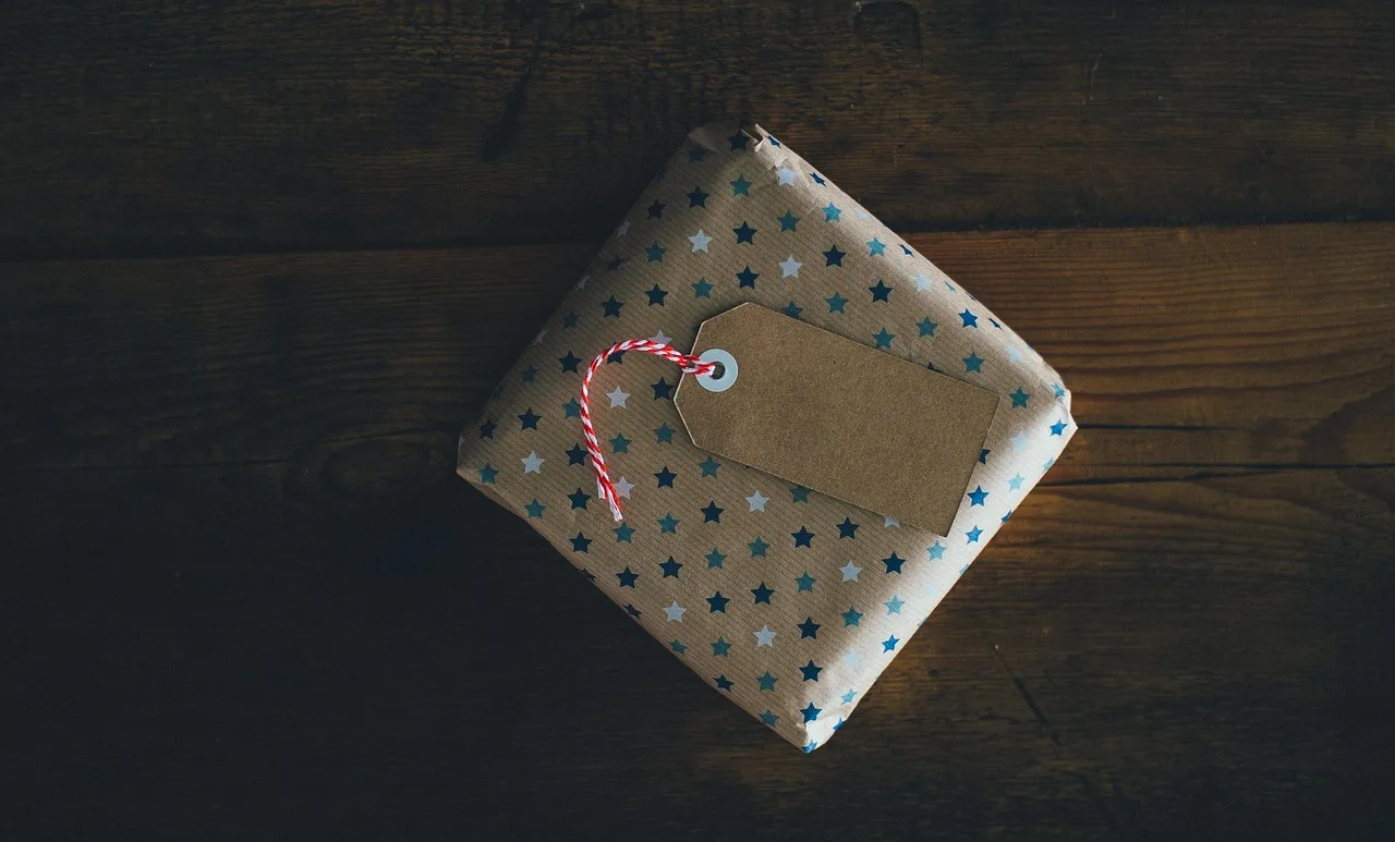 Un paquete envuelto en papel con estrellas y una etiqueta en blanco atada con hilo sobre una mesa de madera oscura