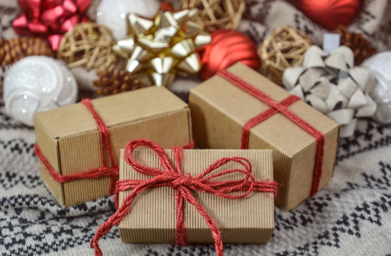Tres paquetes envueltos en papel kraft y atados con hilo rojo entre adornos navideños sobre un tejido