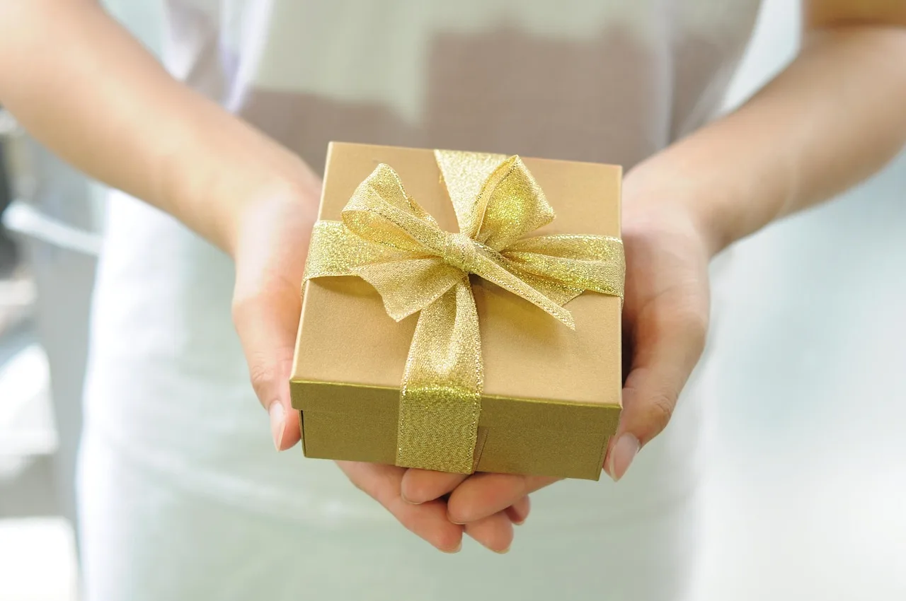 Unas manos sostienen una caja de regalo pequeña atada con una cinta dorada