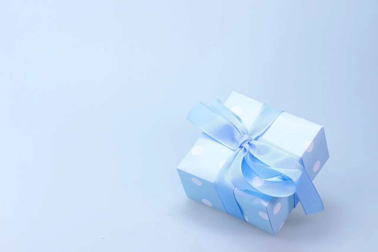 Una caja de regalo celeste con lunares blancos y un moño de cinta apoyada sobre un fondo claro