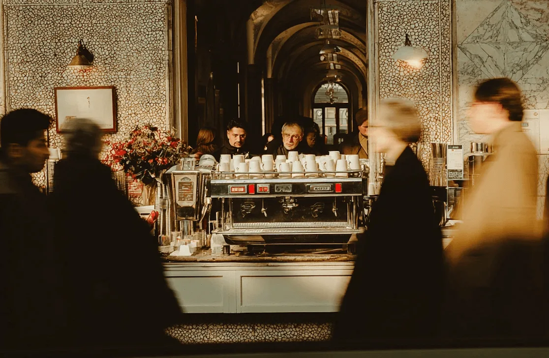 La barra de una cafetería de especialidad con la máquina de espresso y gente esperando