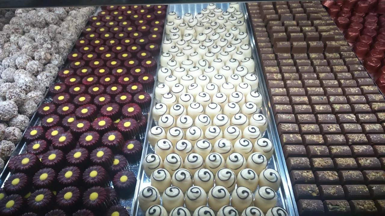 Una vitrina con bandejas de bombones blancos, oscuros y de coco ordenados en filas