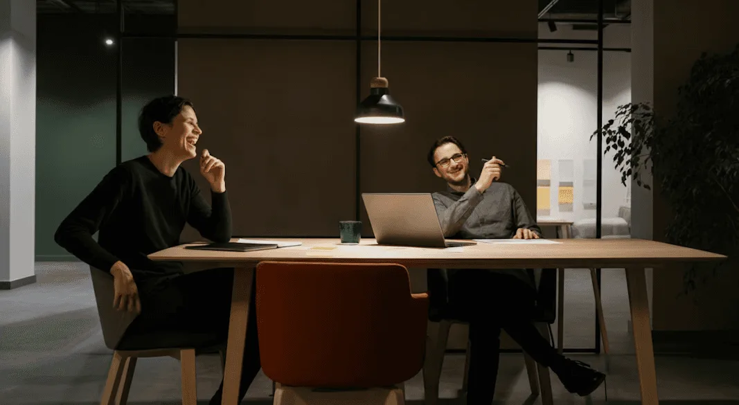Dos personas conversan sentadas en una sala de reuniones en penumbra