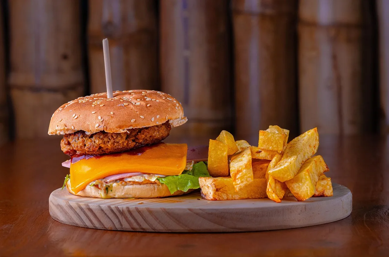 Una hamburguesa con queso y papas fritas servida sobre una tabla de madera en un restaurante de luz cálida