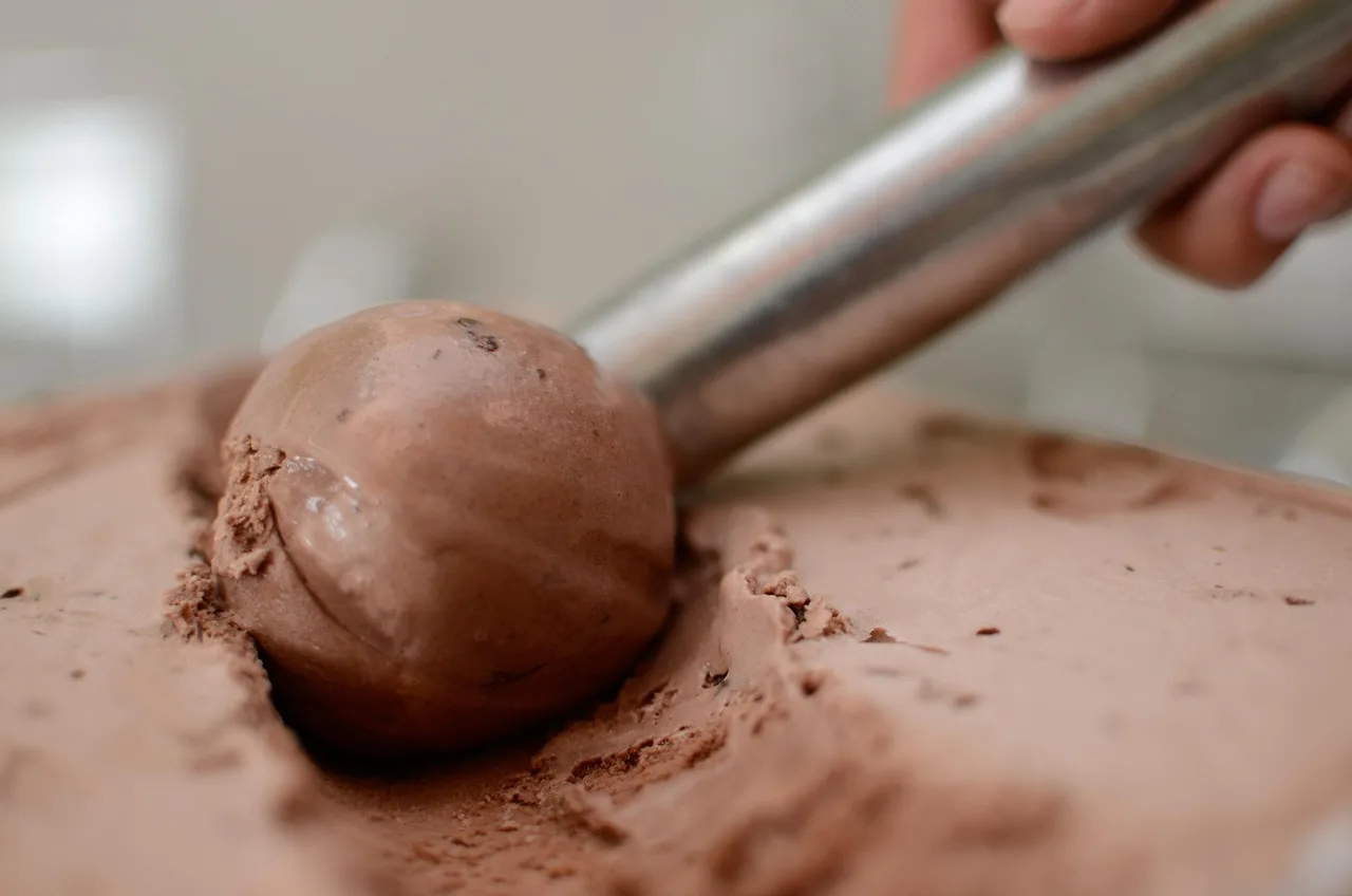 Una cuchara de metal saca una bola de helado de chocolate de una bandeja recién empezada