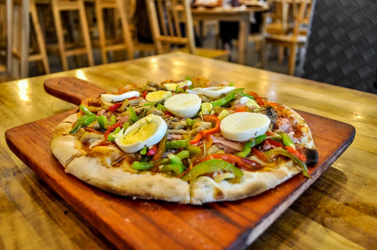 Una pizza con huevo y pimientos servida sobre una tabla de madera en el comedor de un restaurante