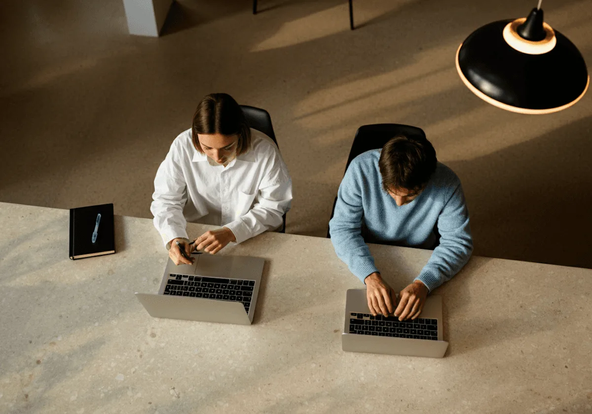 Dos personas trabajan con sus notebooks en un escritorio compartido