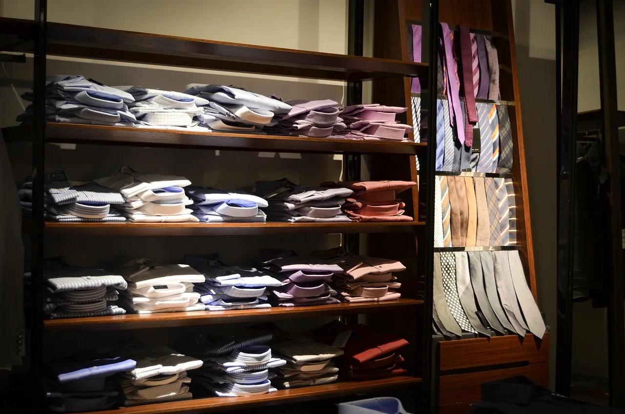 Camisas dobladas y ordenadas en los estantes de madera de una tienda en penumbra, con corbatas al costado
